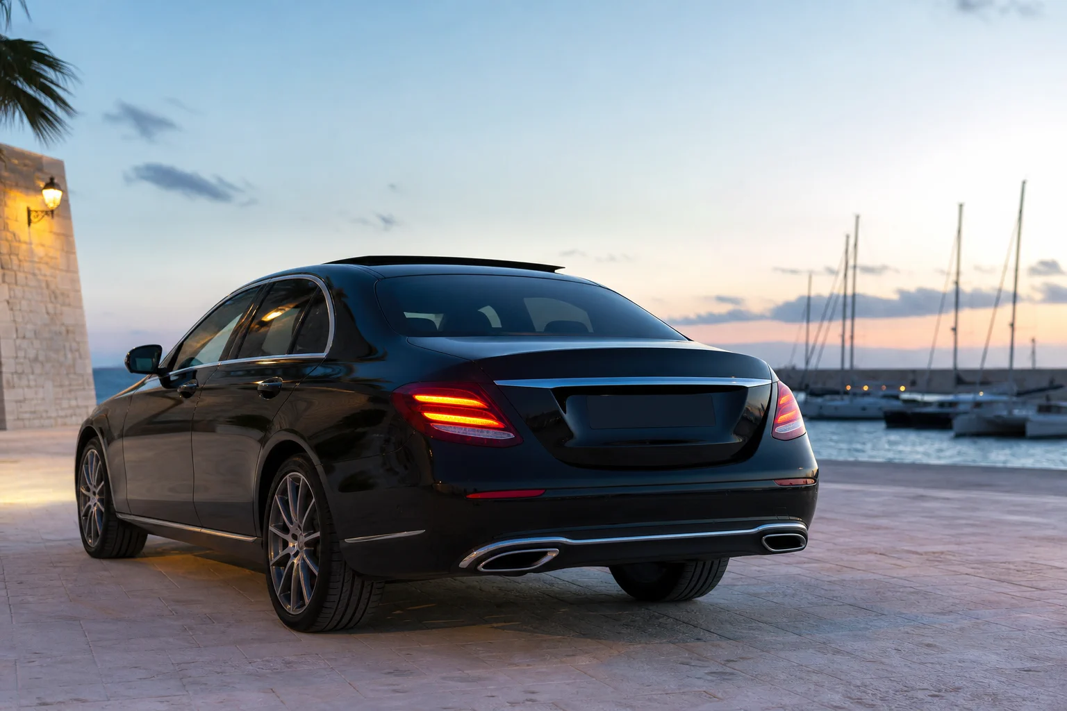 Black Mercedes-Benz E-Class, rear three-quarter view, in a Mediterranean marina setting.