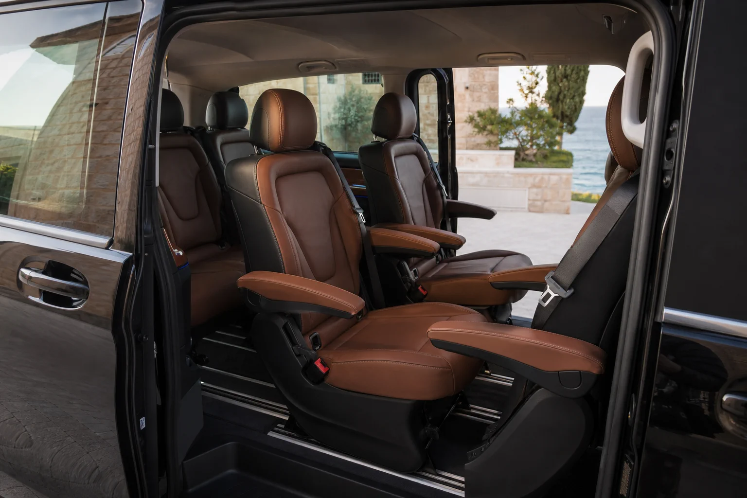 Black Mercedes-Benz V-Class, spacious passenger cabin through an open sliding door, in soft Cyprus coastal light.